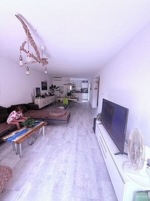 Ein modernes Wohnzimmer mit Flachbildfernseher, einem Essbereich mit Stühlen und einer Küche im Hintergrund.