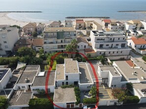 A coastal residential area with multiple buildings, some with flat roofs and others with sloped roofs, and a beach in the background. - Large family home with spacious, landscaped terraces, 100 meters from the beach (Mauguio)