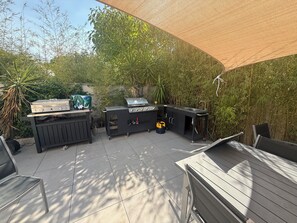 Eine Terrasse im Freien mit Grill, Spüle und Tisch mit Stühlen.