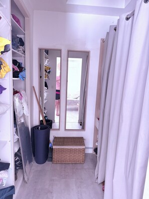 Ein schmaler Flur mit einem Kleiderschrank, einem Spiegel, einem Mülleimer und einem Korbwäscheschrank.