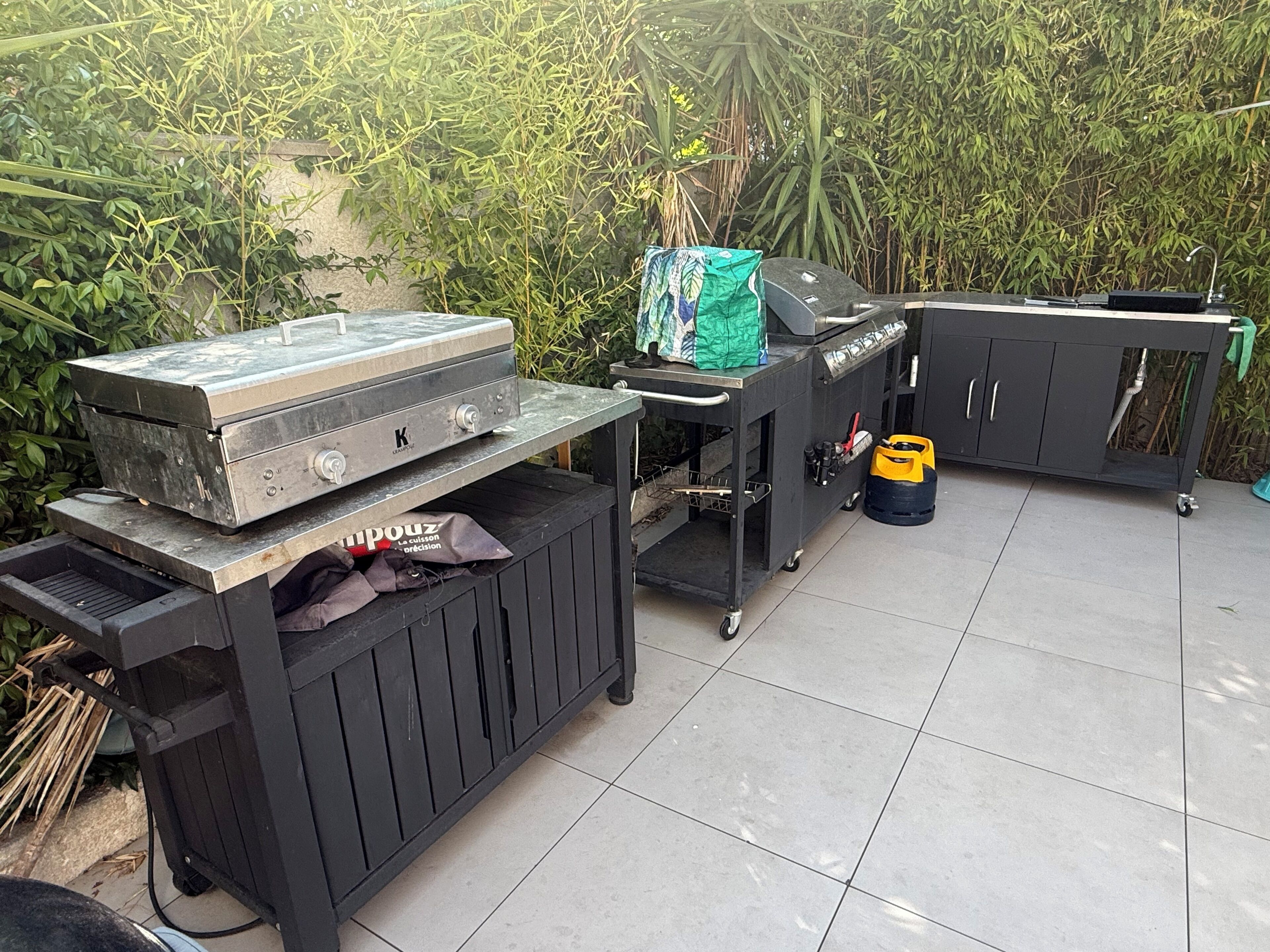 Ein Grillplatz mit Grill, Wagen mit Stauraum und Gasflasche.