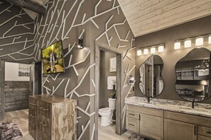 A bathroom with a modern design, featuring a wooden vanity, a large mirror, and a wall-mounted TV. - Lazy River, Pool, Theater, Arcade, Golf Sim, Views (Sevierville)