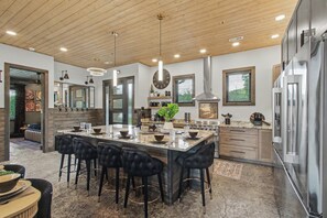 A modern kitchen with a central island, black bar stools, stainless steel appliances, and a wooden ceiling. - Lazy River, Pool, Theater, Arcade, Golf Sim, Views (Sevierville)
