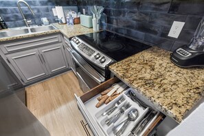 Cozinha com bancada de granito, eletrodomésticos de aço inoxidável e organizador de gaveta com utensílios.