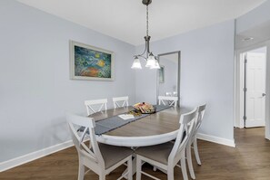 Ein Esszimmer mit einem runden Tisch, weißen Stühlen, einer Kristallleuchter und einem Gemälde an der Wand.