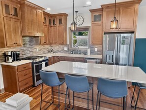 A modern kitchen with wooden cabinets, a stainless steel refrigerator, a large island with bar stools, and a hanging light fixture. - 4BR cabin with hot tub, lake access, and excellent lake view (Bryson City)