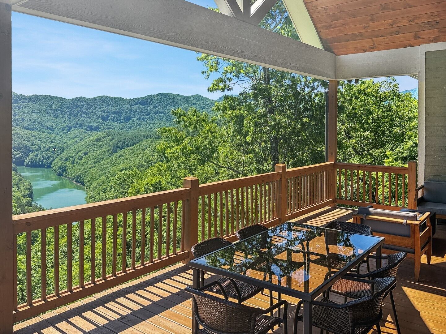 A covered outdoor deck with a table and chairs, overlooking a forested valley.