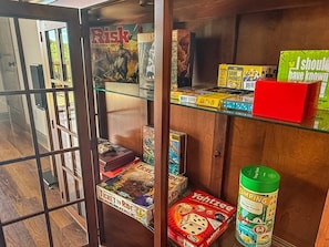 A room with a glass partition, a wooden shelf with various board games, and a green camping puzzle on the floor. - 4BR cabin with hot tub, lake access, and excellent lake view (Bryson City)