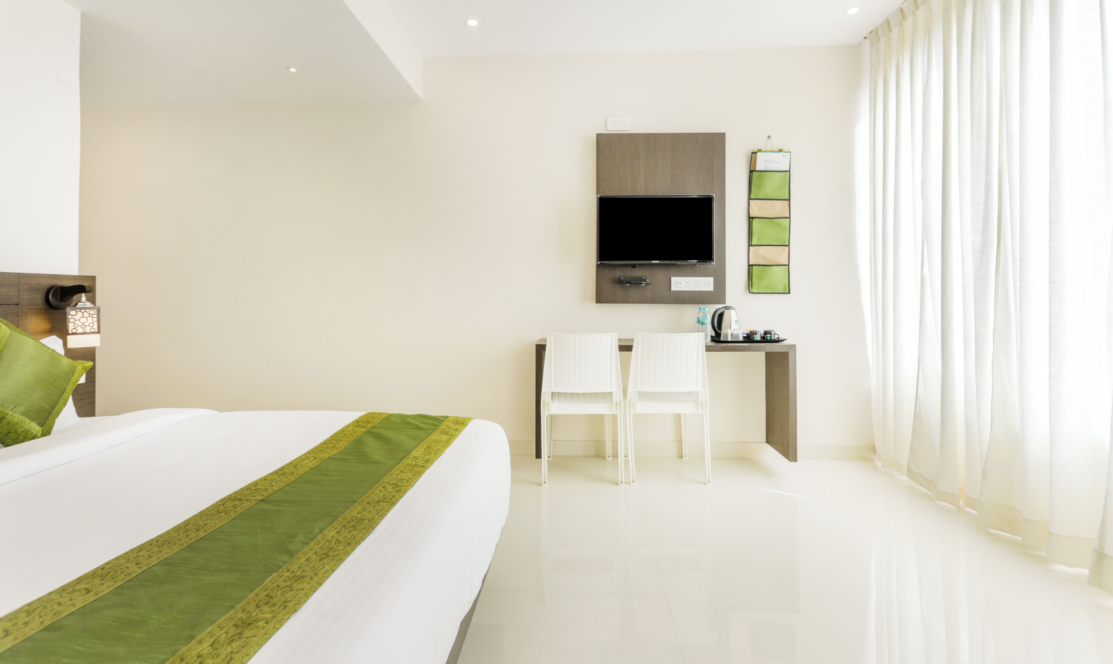 A hotel room with a bed, a desk, a chair, a television, and a window with curtains.