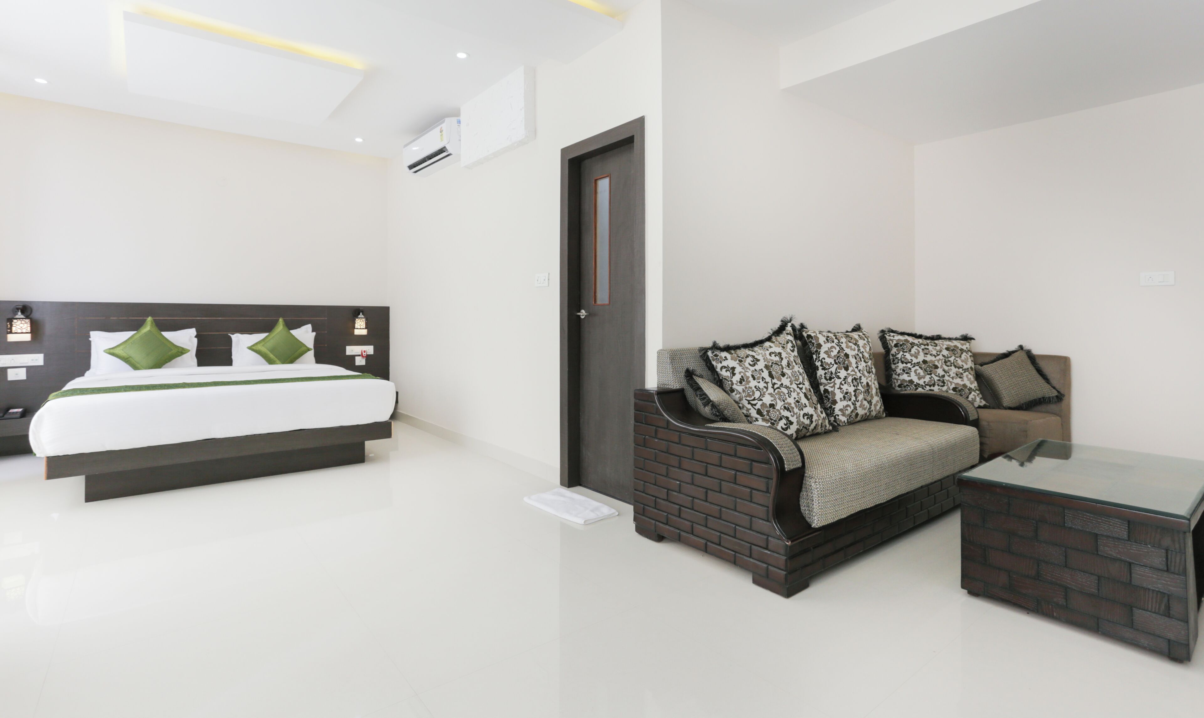 A modern hotel room with a bed, a sofa, a coffee table, and a door.