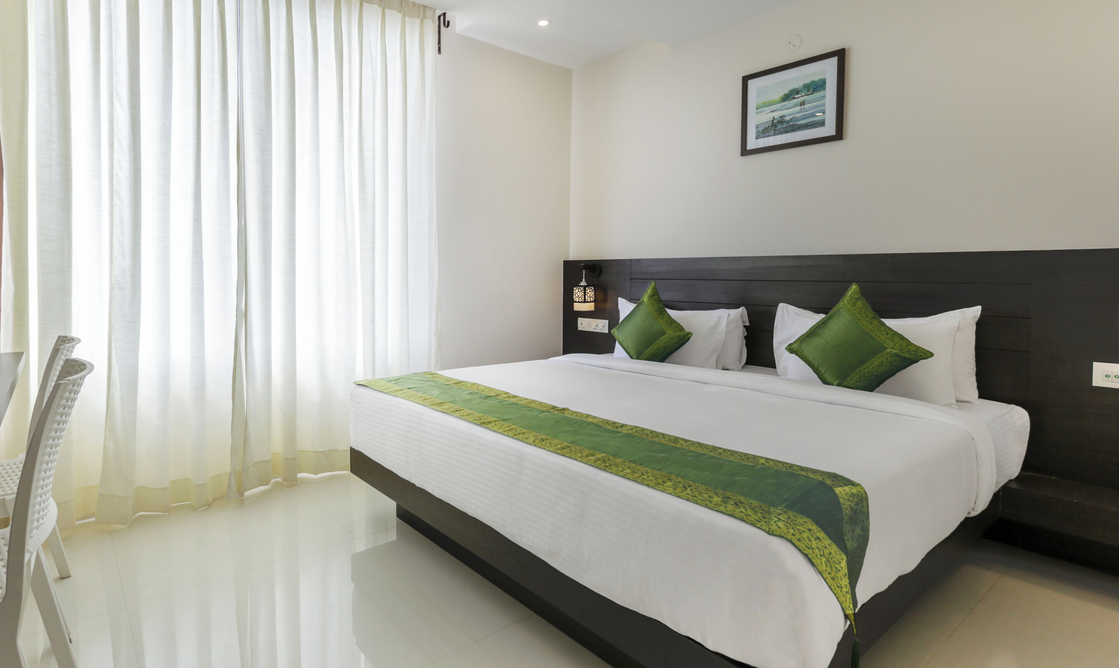 Habitación de hotel con una cama grande, una mesita de noche, una lámpara de pared y un cuadro enmarcado.