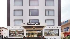 A multi-story hotel with a modern facade, large windows, and a signboard with text. - Hotel Sunrise Luxury Stays (Chikkamagaluru)