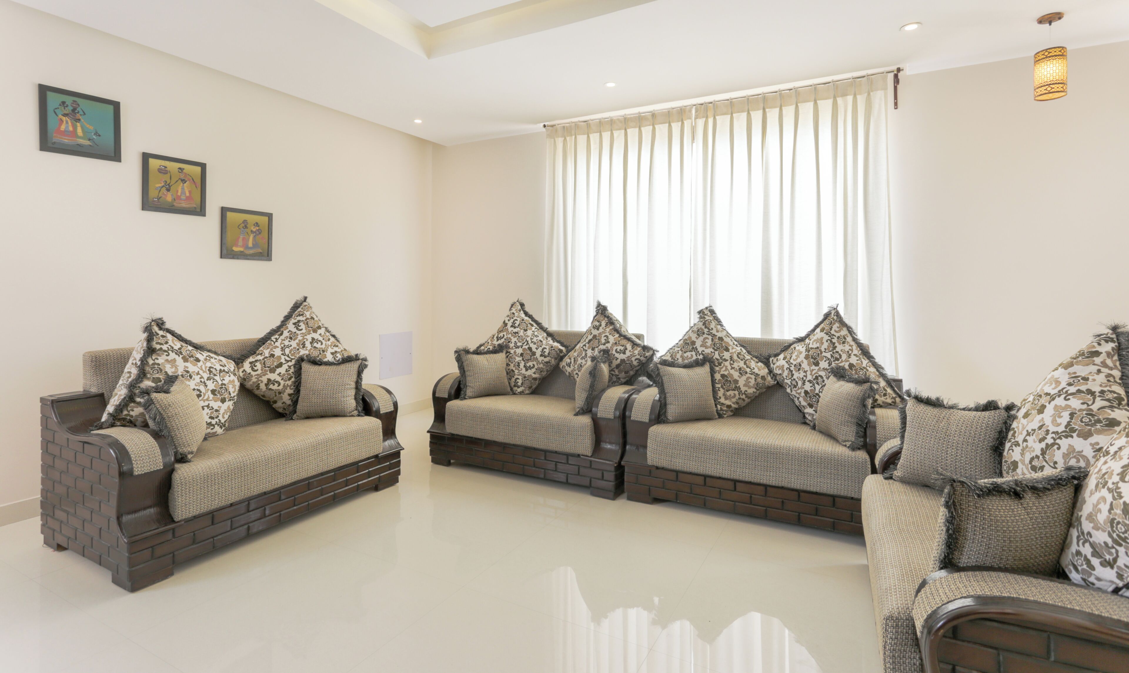 A spacious living room with two sofas, a large window with curtains, and three framed artworks on the wall.