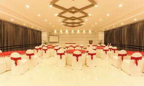 A conference room with round tables and chairs, a podium, and a screen. - Hotel Sunrise Luxury Stays (Chikkamagaluru)