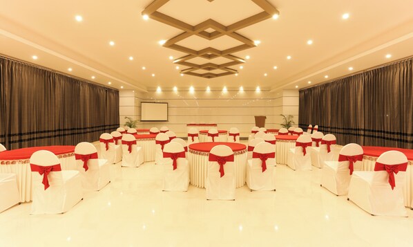A conference room with round tables and chairs, a podium, and a screen.