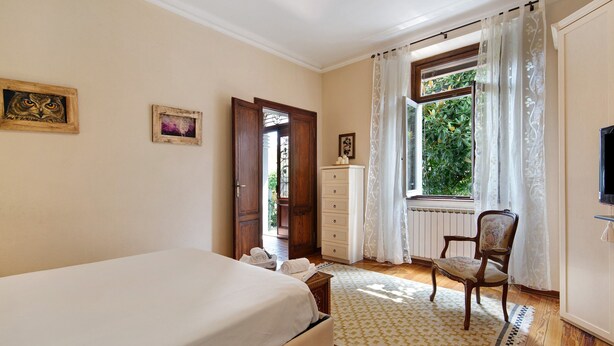 Une chambre à coucher avec un lit, une chaise, une commode et une fenêtre avec des rideaux.