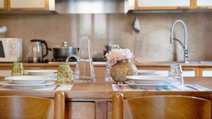Une cuisine avec une table à manger dressée pour deux personnes, un four à micro-ondes, une bouilloire et un vase rempli de fleurs.