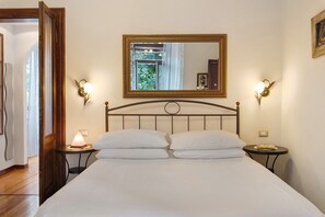 A hotel room with a bed, two bedside tables, a nightstand, a mirror, and wall sconces.