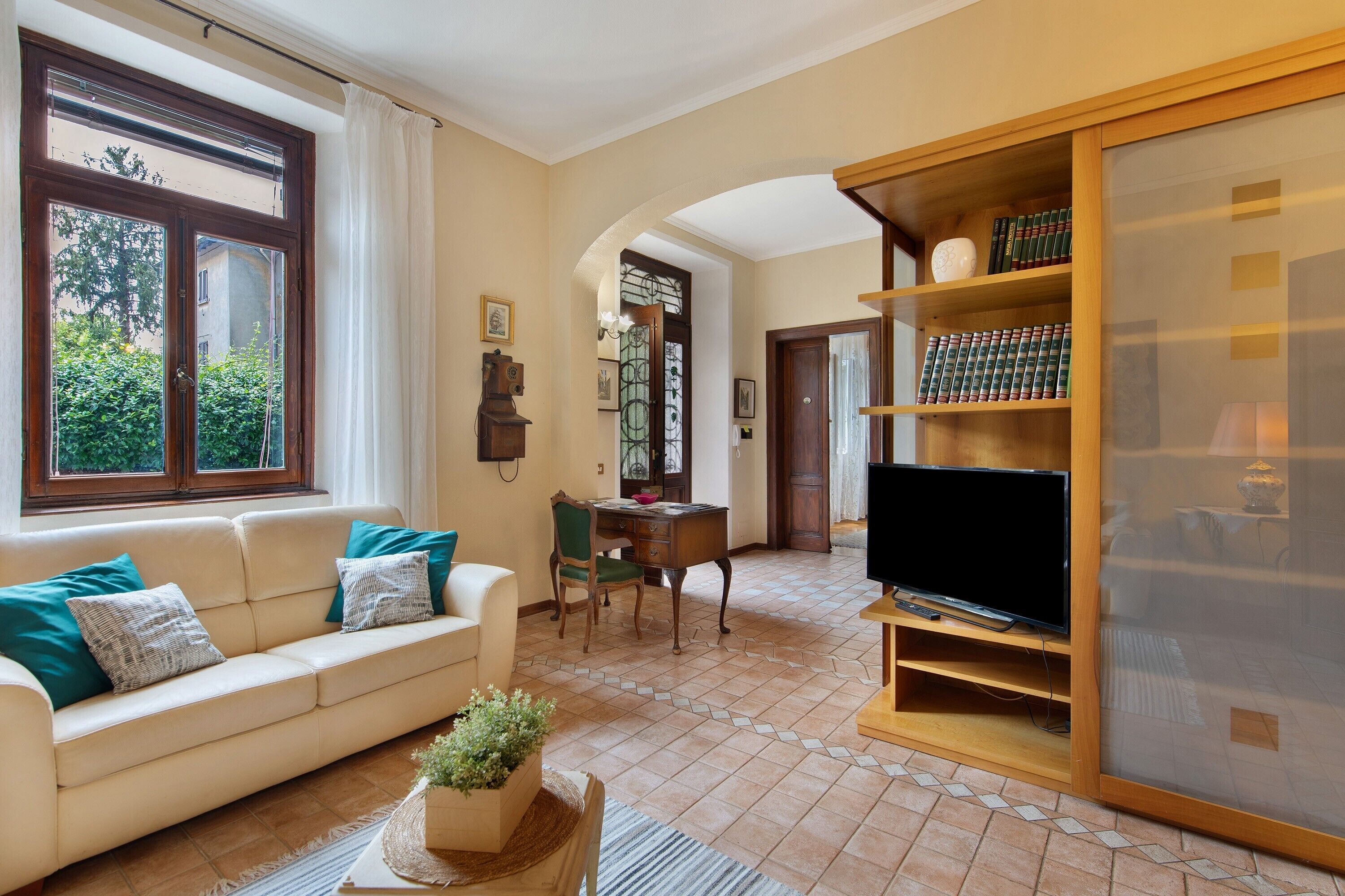 Ein Wohnzimmer mit einer Couch, einem Fernseher, einem Bücherregal und einem Fenster mit Vorhängen.