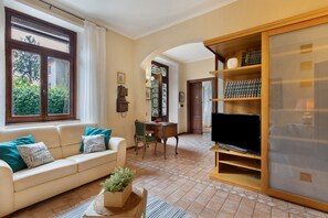 A living room with a sofa, a television, a bookshelf, and a window with curtains.