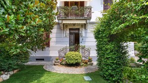 Un jardin bien entretenu, avec un arbuste central, un chemin de pierres et un bâtiment doté d’un balcon.
