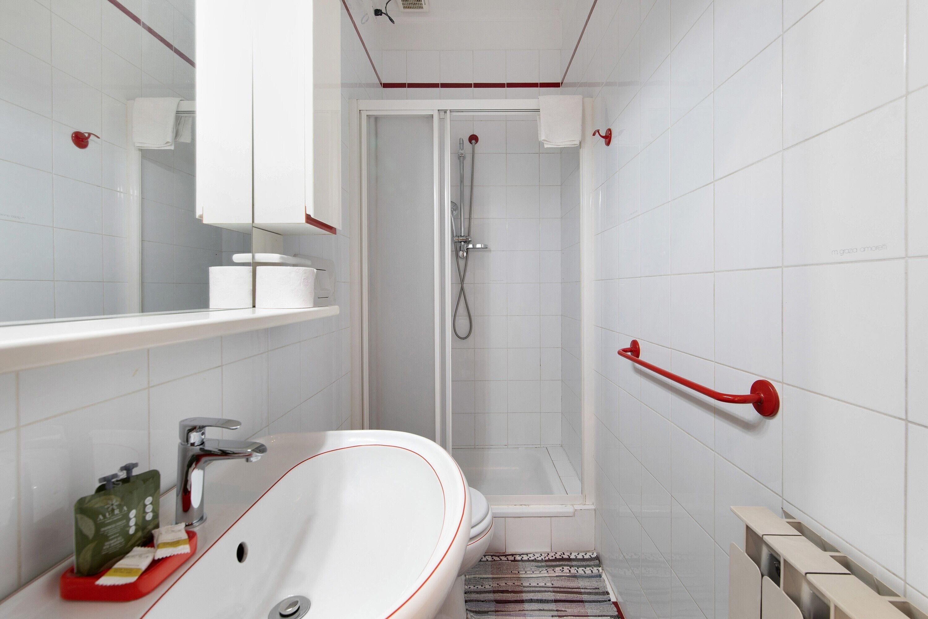 Un bagno moderno con un lavandino bianco, uno specchio, una doccia e un portasciugamani rosso.
