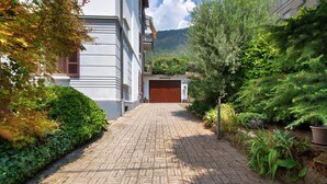 Un chemin pavé mène à un bâtiment dont la porte est fermée, le tout étant entouré d’une végétation luxuriante et ayant une chaîne de montagnes en arrière-plan.