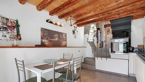 A modern kitchen with a dining area, wooden ceiling beams, a stone wall, and a kitchen island.