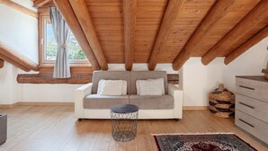 A room with a wooden ceiling, a sofa with cushions, a small round table, a patterned rug, and a wicker basket.
