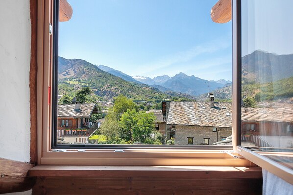 A window with a view of a mountainous landscape, a wooden window frame, and a clear sky.