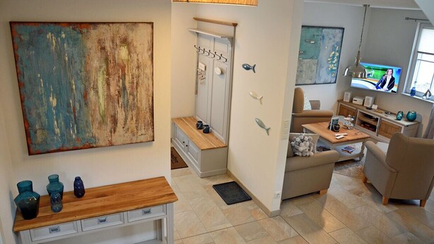 A modern living room with a sofa, a coffee table, and a television. There is a wooden bench with decorative vases and a painting on the wall. - Vacation home with a fireplace and sauna, about 600 meters from the sandy beach; pets welcome (Glowe)