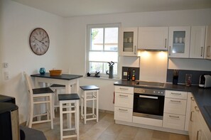 A kitchen with white cabinets, a black countertop, a stove, and a clock on the wall. - Vacation home with a fireplace and sauna, about 600 meters from the sandy beach; pets welcome (Glowe)