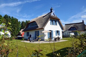 Ein Haus mit einem Strohdach, einer weißen Fassade und blauen Fensterläden.