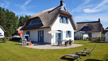 A house with a thatched roof, a patio with outdoor furniture, and a lawn.