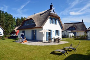 A house with a thatched roof, a patio with outdoor furniture, and a lawn. - Vacation home with a fireplace and sauna, about 600 meters from the sandy beach; pets welcome (Glowe)