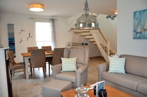 Un salón moderno con comedor, una escalera y vista al mar.