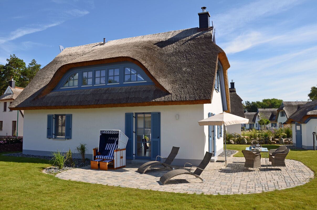 A house with a thatched roof, a covered patio with seating, and a visible window.