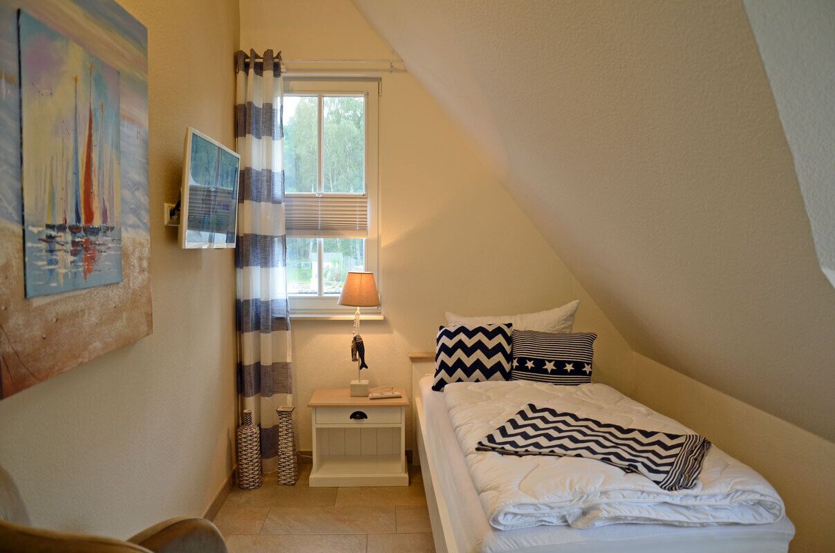 A bedroom with a bed, a nightstand, a lamp, a window with curtains, and a painting on the wall.