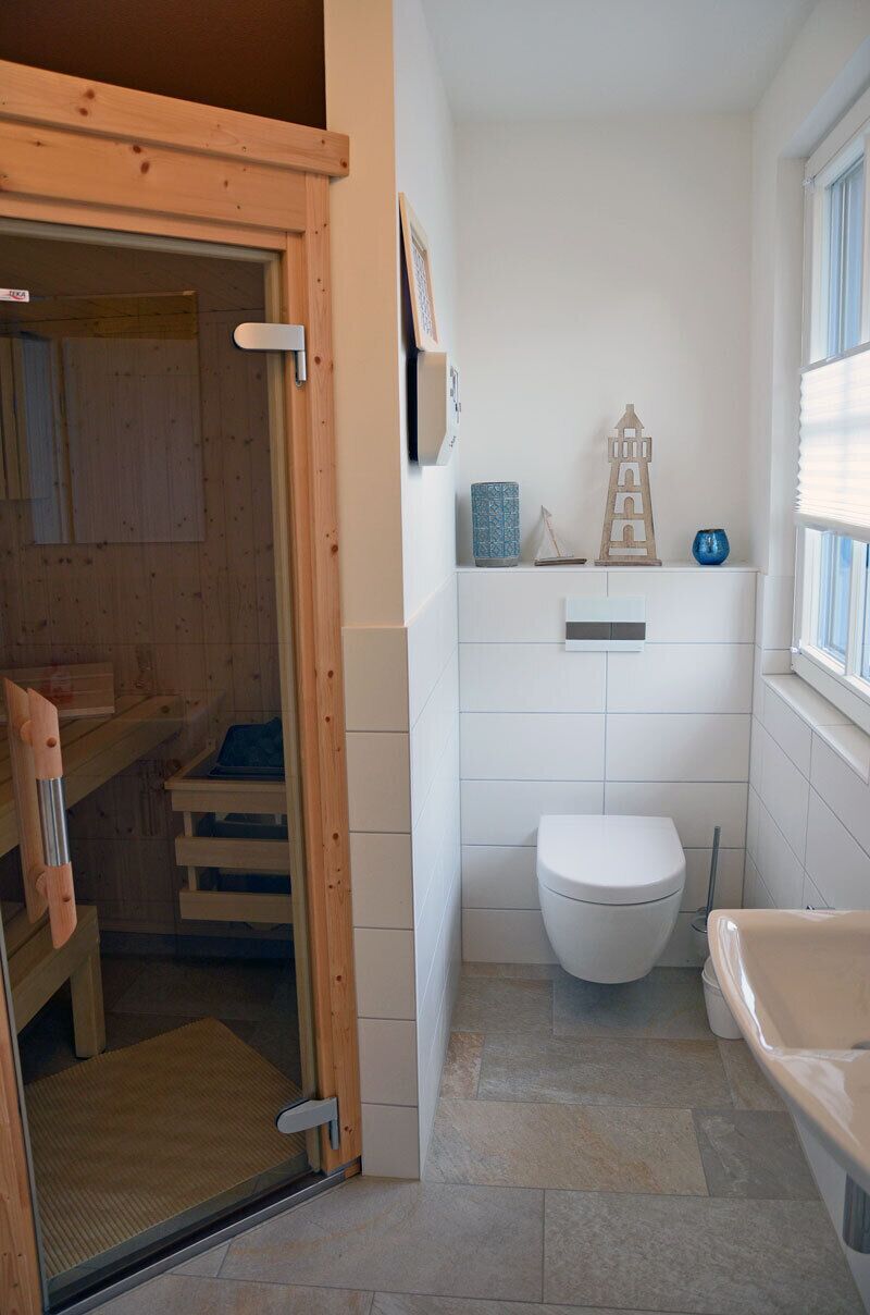 A compact bathroom with a toilet, a small shelf with decorative items, and a window.
