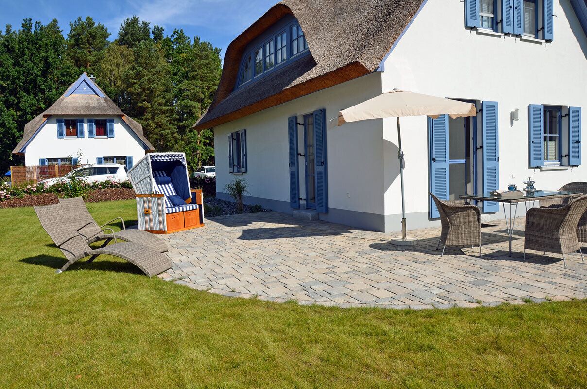 Une maison avec un toit de chaume, une terrasse dallée et du mobilier d’extérieur.