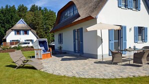 A house with a thatched roof, a paved patio, and outdoor furniture. - Vacation home with a fireplace and sauna, about 600 meters from the sandy beach; pets welcome (Glowe)