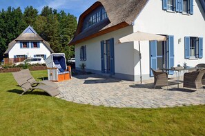 Ein Haus mit Strohdach, einer gepflasterten Terrasse und Gartenmöbeln.