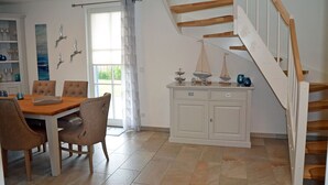 A dining area with a wooden table and chairs, a white cabinet with decorative items, and a staircase with wooden steps. - Vacation home with a fireplace and sauna, about 600 meters from the sandy beach; pets welcome (Glowe)