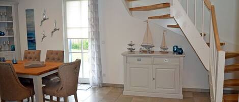 Een eetgedeelte met een houten tafel en stoelen, een wit kastje met decoratieve objecten, en een trap met houten treden.