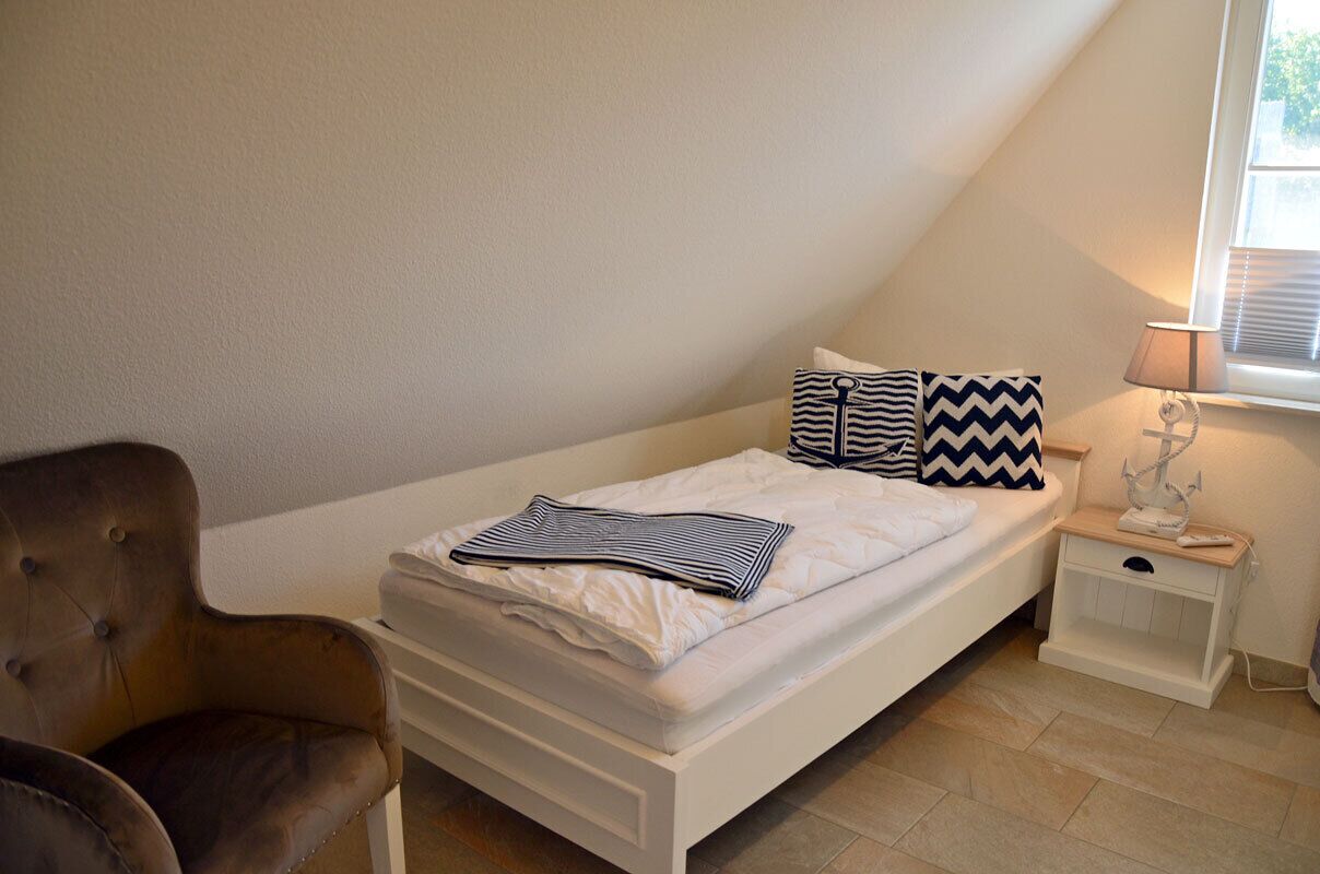 Een slaapkamer met een bed, nachtkastje, lamp en stoel.