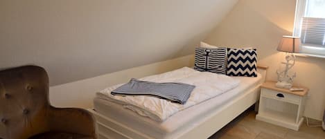 A bedroom with a bed, a nightstand, a lamp, and a chair.