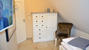 A room with a white wardrobe, a brown chair, and a bed with a striped pillow. - Vacation home with a fireplace and sauna, about 600 meters from the sandy beach; pets welcome (Glowe)