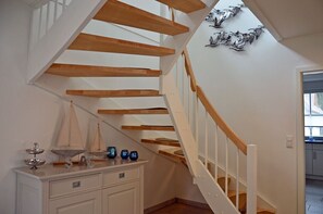 A staircase with wooden beams and white railings, a white dresser with decorative items, and a wall with a metal sculpture. - Vacation home with a fireplace and sauna, about 600 meters from the sandy beach; pets welcome (Glowe)