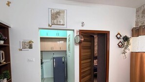 Ein Zimmer mit Fliesenboden, einem blauen Teppich mit Muster, einer Holztür und einer Küchenzeile mit Schränken und einem Kühlschrank.