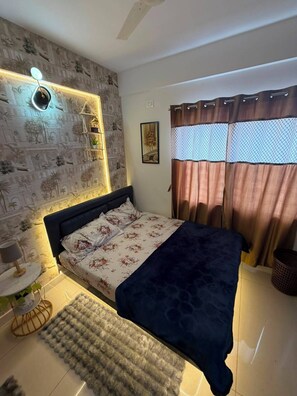 Un dormitorio con cama, mesita de noche, lámpara de pared, ventana con cortinas y pared con diseño.